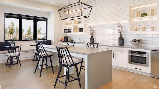 kitchen with a kitchen bar, appliances with stainless steel finishes, decorative light fixtures, white cabinets, and a kitchen island