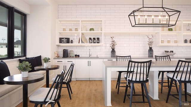 bar featuring sink, hanging light fixtures, light hardwood / wood-style flooring, tasteful backsplash, and white cabinetry