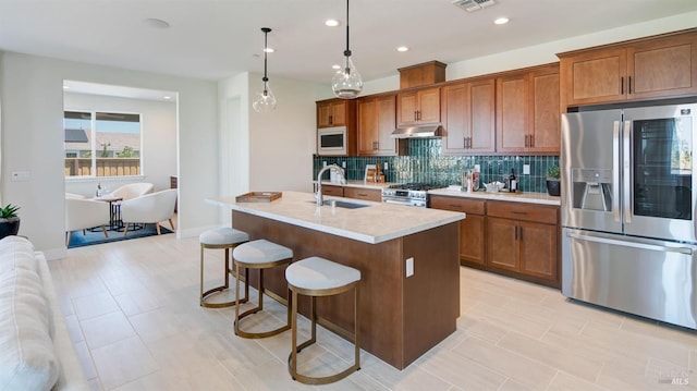 kitchen with sink, tasteful backsplash, decorative light fixtures, a kitchen island with sink, and appliances with stainless steel finishes