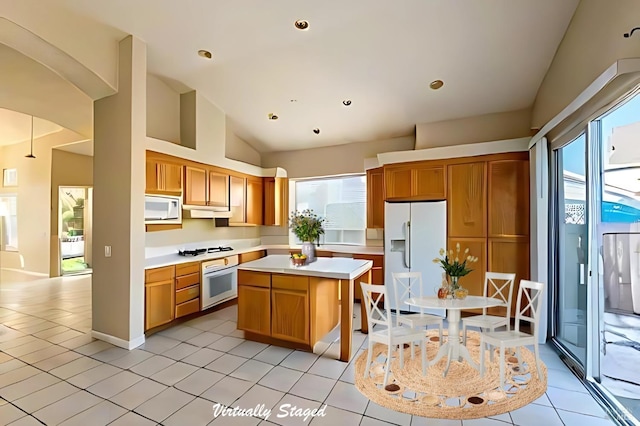 kitchen with vaulted ceiling, a center island, light tile patterned floors, and white appliances