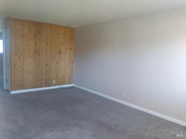 unfurnished room featuring wood walls and dark carpet