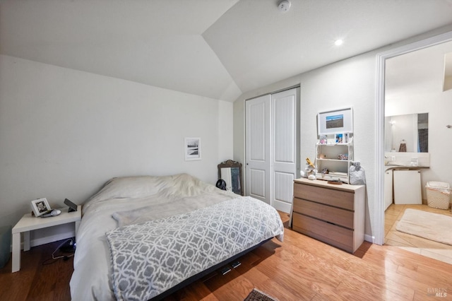 bedroom with lofted ceiling, light hardwood / wood-style flooring, and a closet