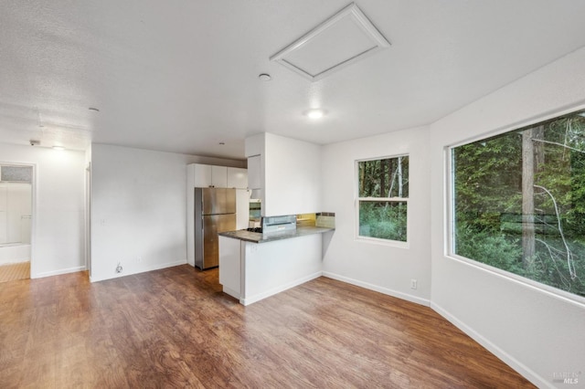 kitchen featuring kitchen peninsula, wood-type flooring, white cabinetry, and stainless steel refrigerator