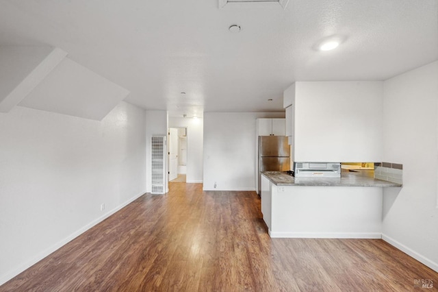 kitchen featuring stainless steel refrigerator, white cabinetry, kitchen peninsula, and wood-type flooring