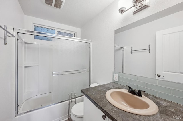 full bathroom featuring vanity, backsplash, combined bath / shower with glass door, toilet, and a textured ceiling