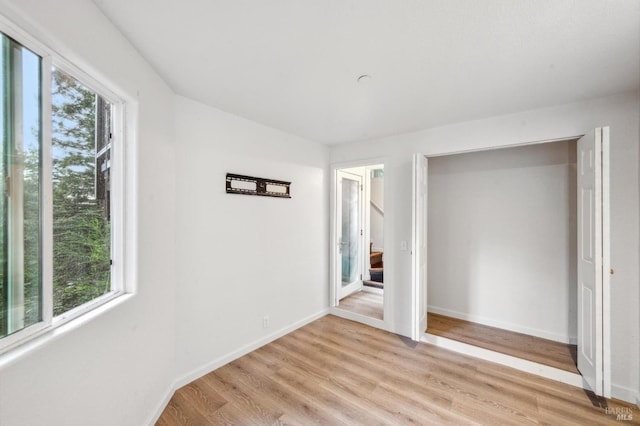 unfurnished bedroom with a closet, light wood-type flooring, and multiple windows