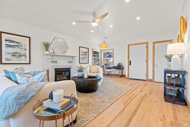 living room with ceiling fan, light wood-type flooring, and a high end fireplace