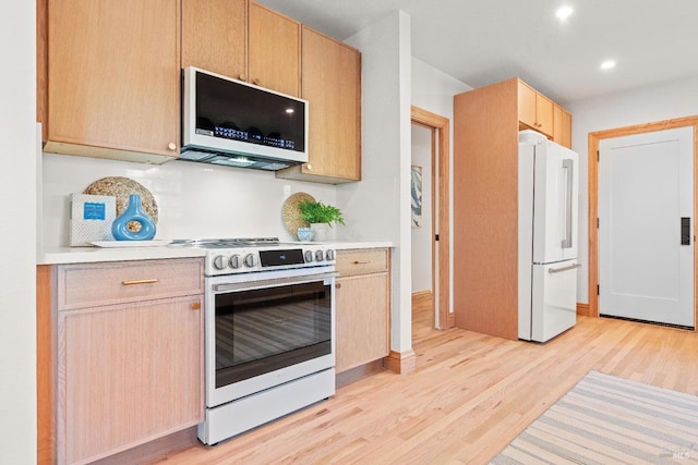 kitchen featuring light brown cabinetry, white appliances, and light hardwood / wood-style flooring