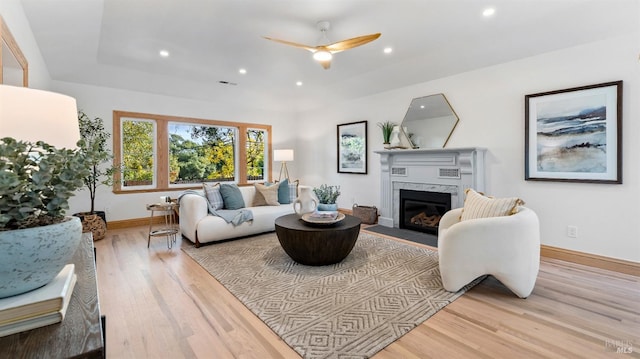 living room with light hardwood / wood-style floors, ceiling fan, and a premium fireplace