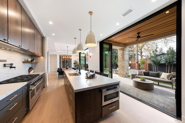 kitchen featuring a kitchen island with sink, sink, dark brown cabinets, light hardwood / wood-style floors, and stainless steel appliances