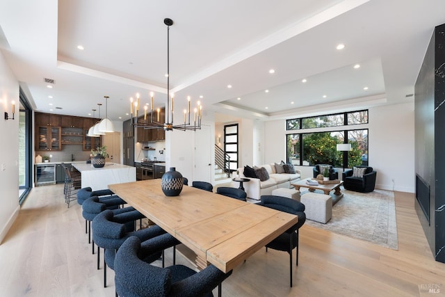 dining space with an inviting chandelier, light hardwood / wood-style flooring, a raised ceiling, and beverage cooler