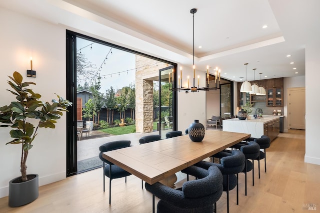 dining space with sink, light hardwood / wood-style floors, a tray ceiling, and a notable chandelier