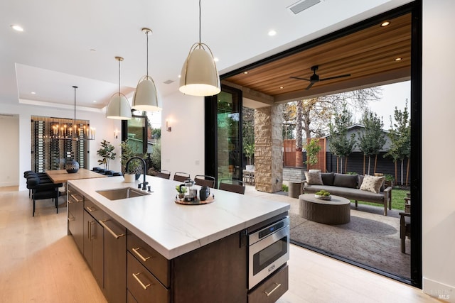 kitchen featuring light wood-type flooring, dark brown cabinetry, sink, stainless steel microwave, and an island with sink