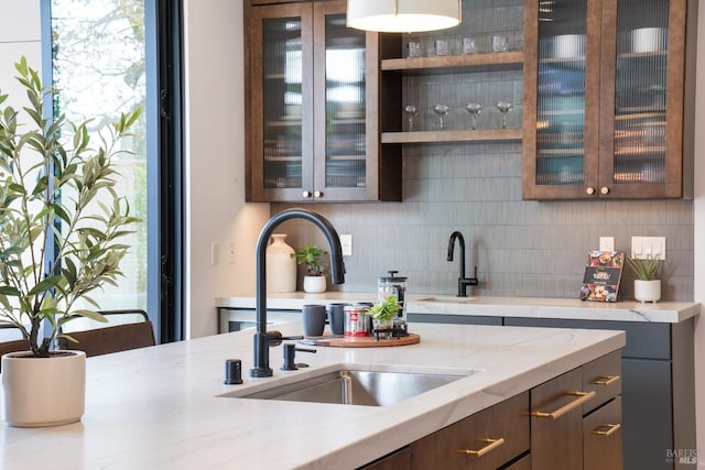 kitchen featuring light stone countertops, dark brown cabinets, backsplash, and sink