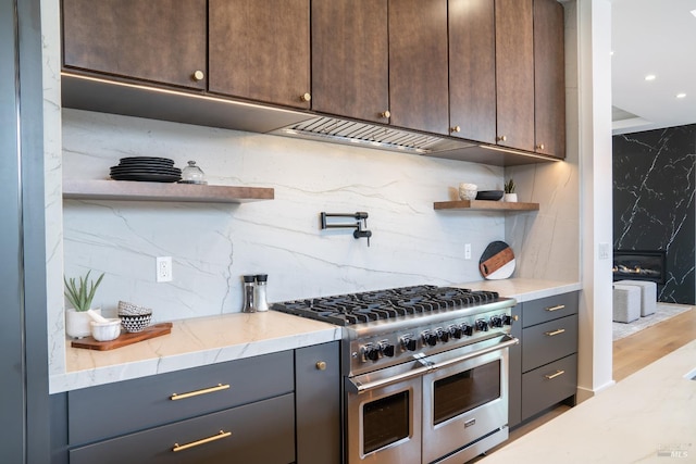 kitchen featuring light stone countertops, dark brown cabinets, backsplash, and range with two ovens