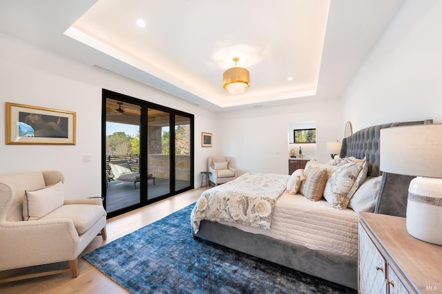 bedroom featuring access to outside, a tray ceiling, and light wood-type flooring