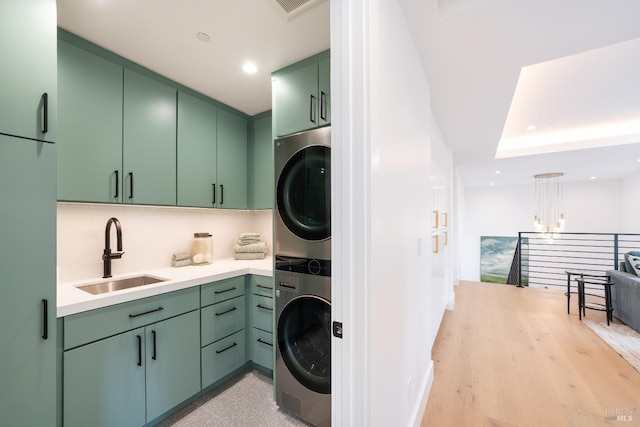 washroom featuring sink, cabinets, a notable chandelier, light hardwood / wood-style floors, and stacked washer and clothes dryer