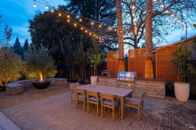 patio terrace at dusk featuring area for grilling, an outdoor fire pit, and grilling area