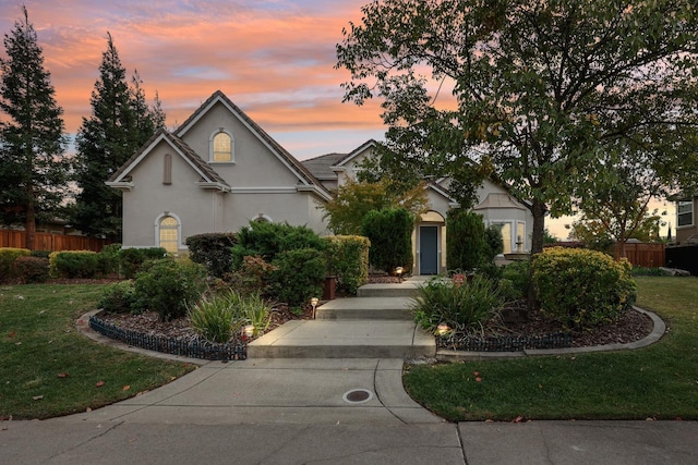 view of front facade with stucco siding, a lawn, and fence