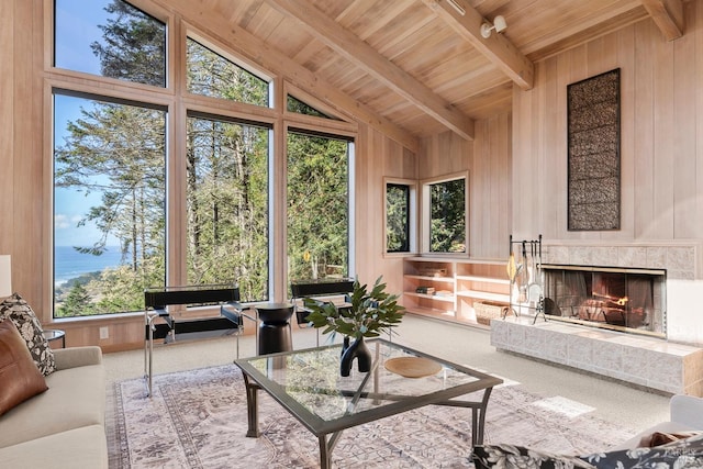 carpeted living room featuring wood ceiling, beam ceiling, high vaulted ceiling, a fireplace, and wood walls