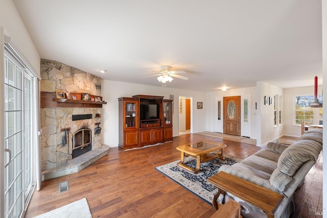 living room featuring hardwood / wood-style flooring, ceiling fan, and a stone fireplace