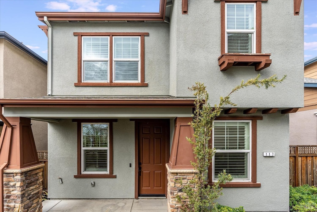 townhome / multi-family property featuring stone siding, fence, and stucco siding