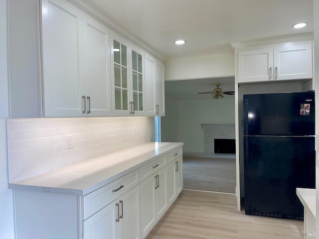 kitchen featuring light wood-type flooring, decorative backsplash, white cabinetry, and black fridge