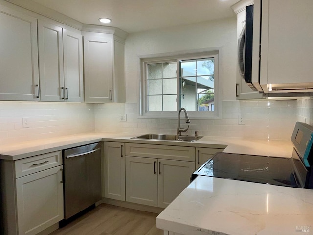 kitchen featuring decorative backsplash, sink, light wood-type flooring, appliances with stainless steel finishes, and light stone counters