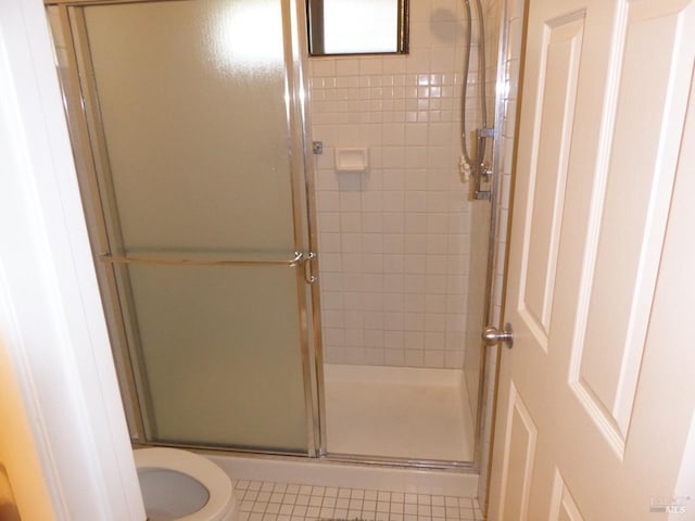 bathroom with tile patterned floors, toilet, and a shower with door