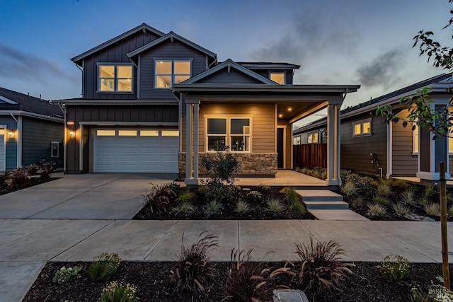 view of front of home with a garage, driveway, stone siding, covered porch, and board and batten siding