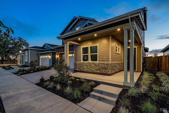 view of front of property with a garage, stone siding, driveway, and fence