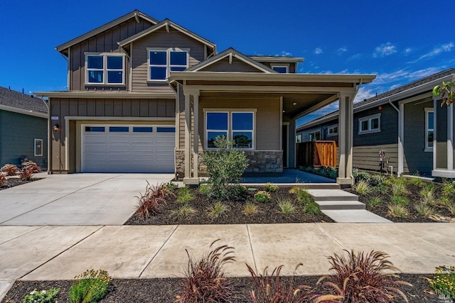 craftsman house featuring covered porch, an attached garage, board and batten siding, stone siding, and driveway