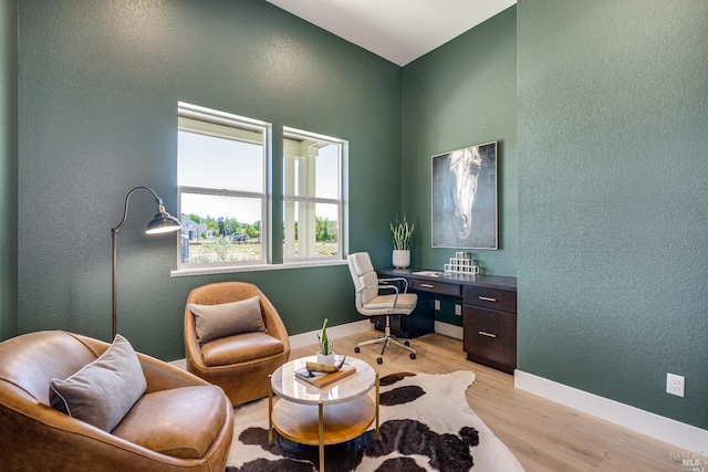 home office featuring baseboards, a textured wall, and light wood-style floors