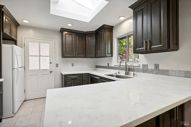 kitchen with white refrigerator, sink, a skylight, light tile patterned floors, and dark brown cabinetry