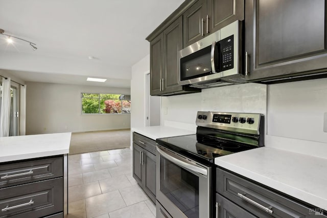 kitchen with dark brown cabinetry, light tile patterned floors, and appliances with stainless steel finishes