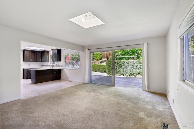 unfurnished living room featuring a skylight, a wealth of natural light, light carpet, and visible vents
