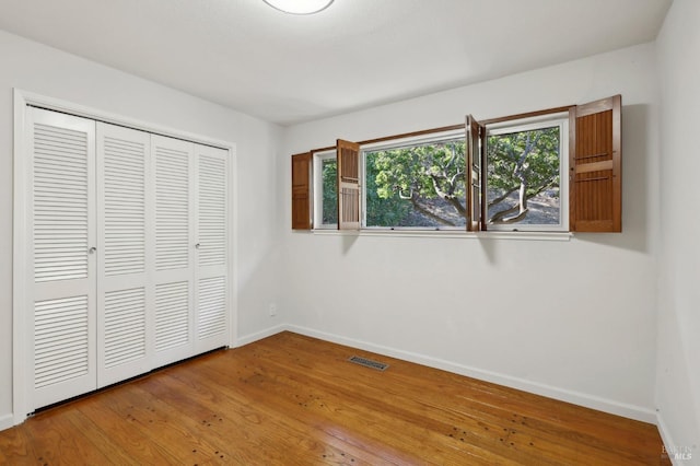 unfurnished bedroom with multiple windows, a closet, and wood-type flooring