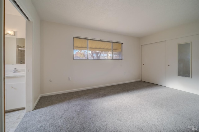 unfurnished bedroom featuring light colored carpet, connected bathroom, a closet, and a textured ceiling