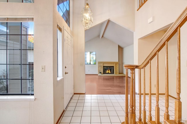 entryway with beam ceiling, a brick fireplace, light hardwood / wood-style flooring, high vaulted ceiling, and a notable chandelier