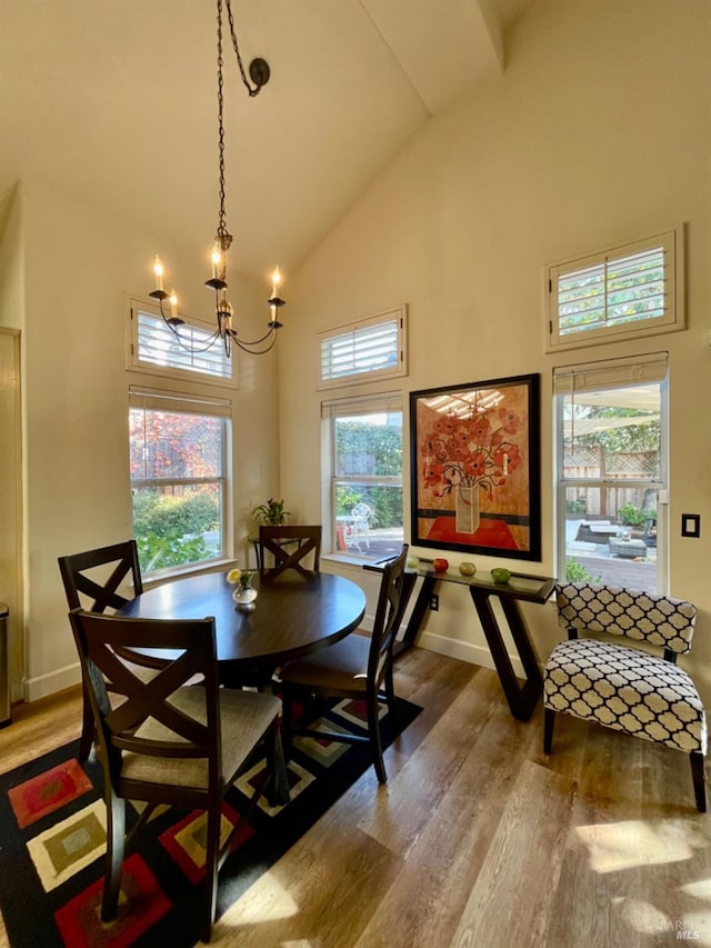 dining space with a wealth of natural light, high vaulted ceiling, wood-type flooring, and an inviting chandelier