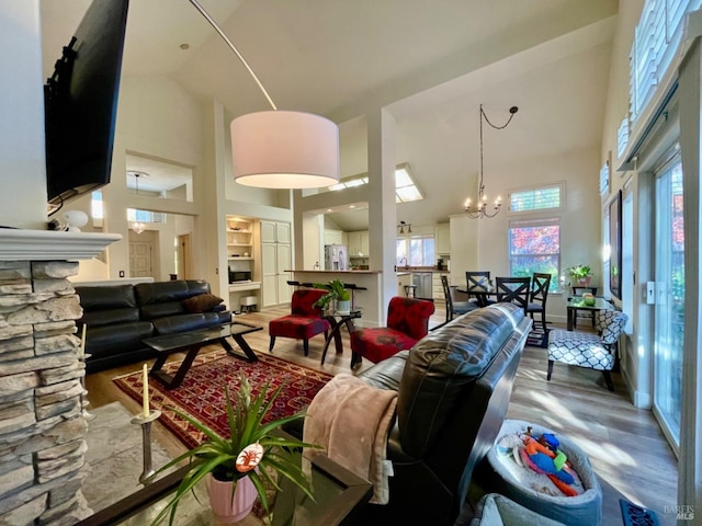 living room with a stone fireplace, high vaulted ceiling, a chandelier, and wood-type flooring