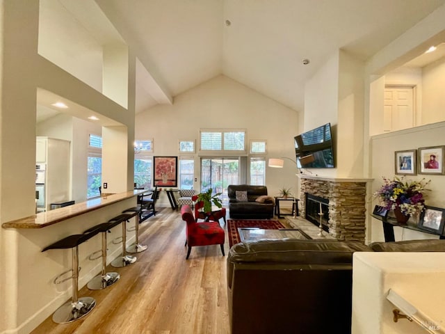 living room featuring a stone fireplace, high vaulted ceiling, and wood-type flooring