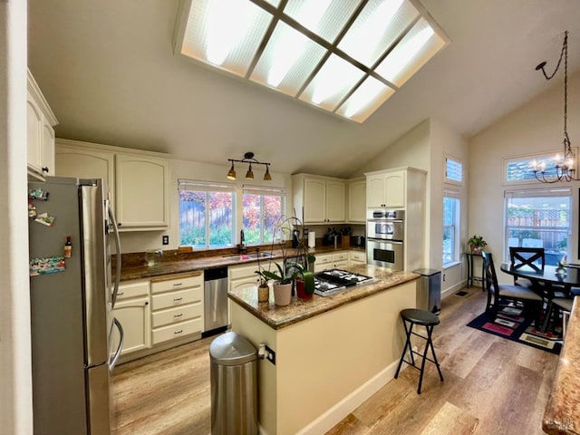 kitchen with a center island, vaulted ceiling, decorative light fixtures, light hardwood / wood-style floors, and stainless steel appliances