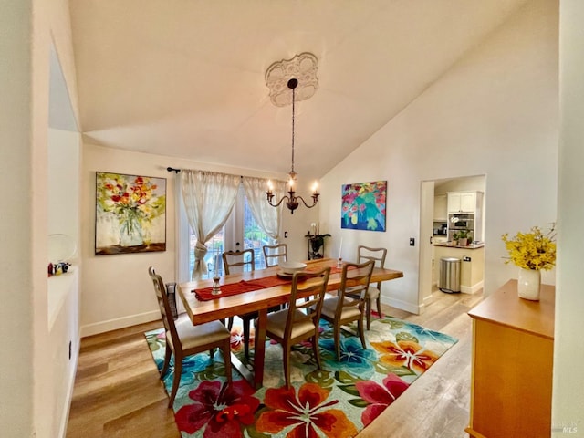 dining space with a chandelier, high vaulted ceiling, and light hardwood / wood-style flooring