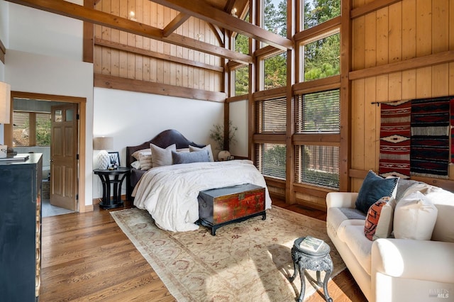 bedroom with wood-type flooring, a towering ceiling, multiple windows, and beam ceiling