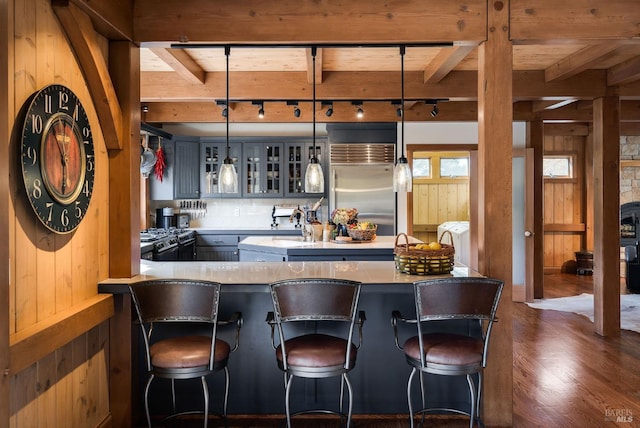 bar featuring wooden walls, dark wood-type flooring, pendant lighting, and appliances with stainless steel finishes