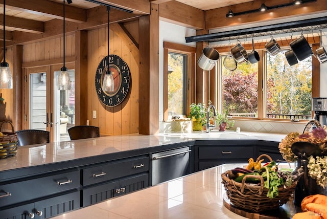 kitchen with sink, hanging light fixtures, wooden walls, stainless steel dishwasher, and beamed ceiling