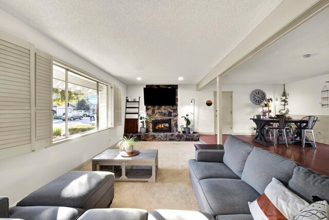 carpeted living room featuring a stone fireplace, beam ceiling, and a textured ceiling