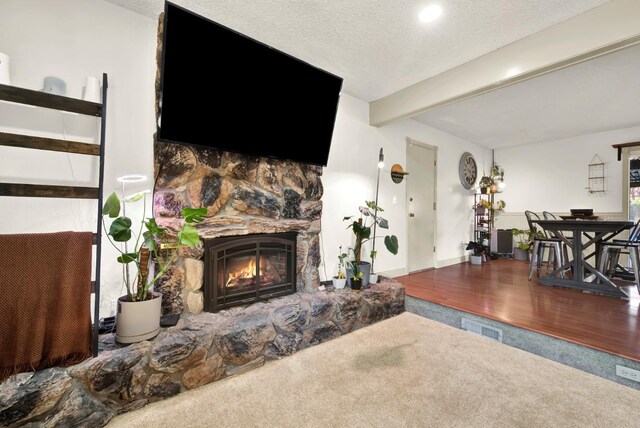 living room with beam ceiling, a stone fireplace, a textured ceiling, and carpet flooring