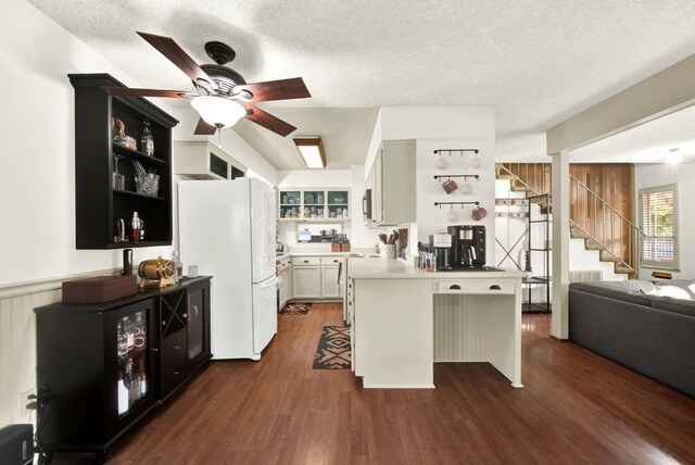 kitchen with dark wood-type flooring, a breakfast bar area, white cabinetry, white refrigerator, and kitchen peninsula